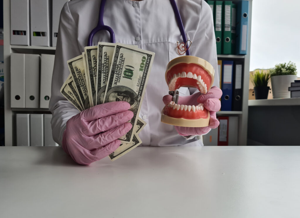 Person holding dollars in one hand and a model of teeth in another