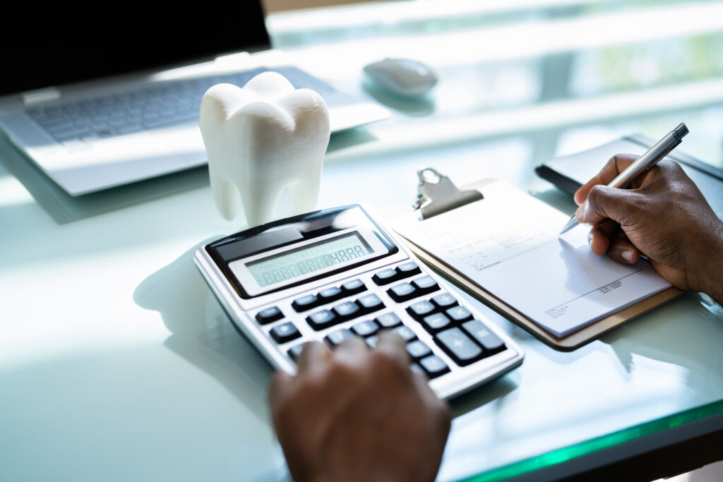 Person writing on paper and using a calculator with a tooth on the table