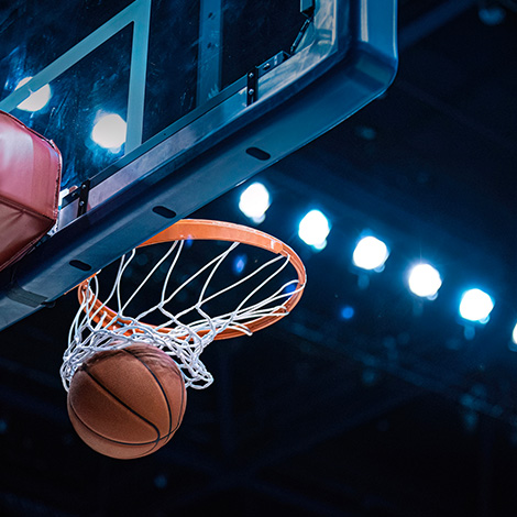 Close up shot of a basketball and basketball ring with stadium lights in the background