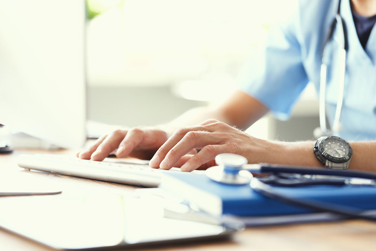 Medicine doctor's writing on keyboard in medical office close-up. Stethoscope, clipboard and notepad on foreground.