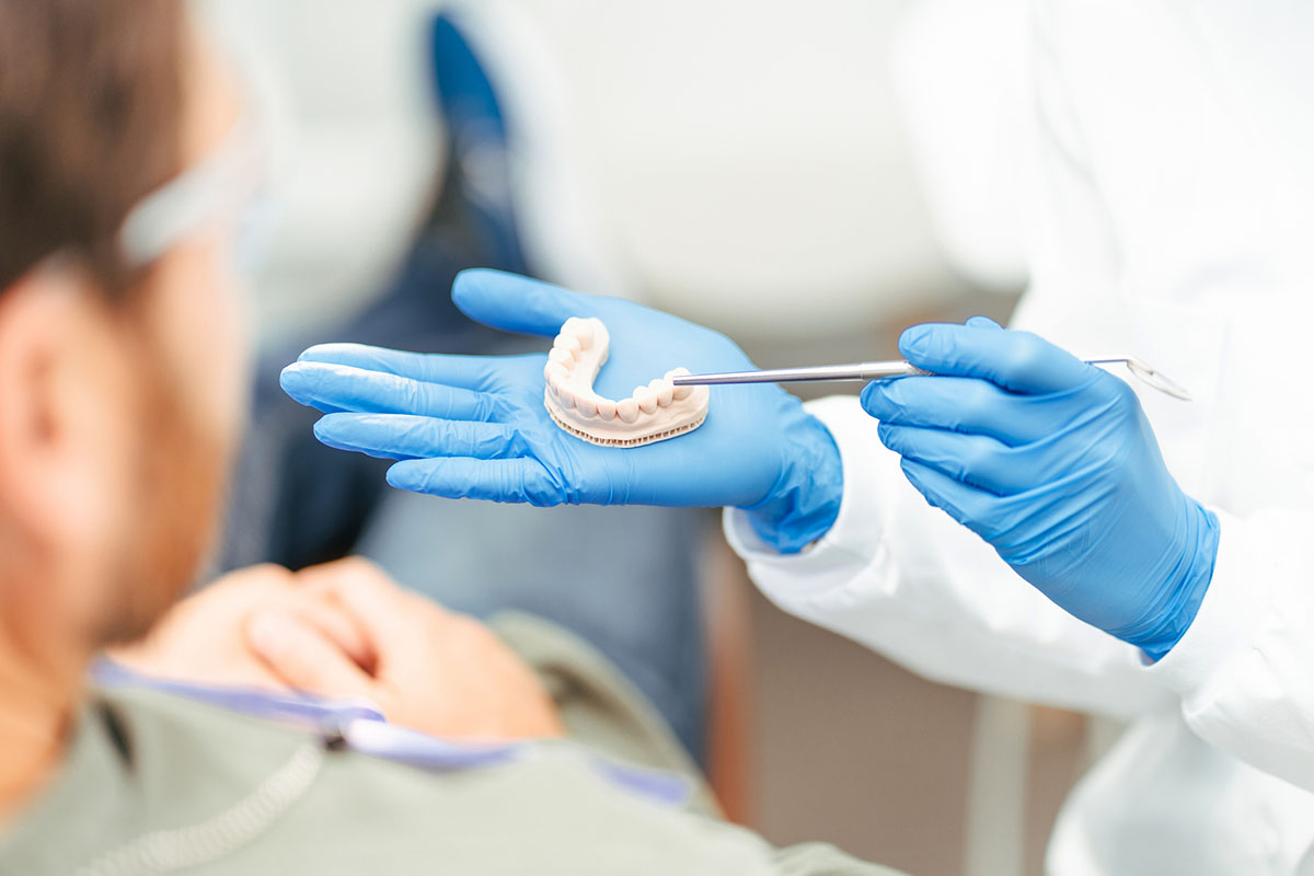 Dentist explaining dental treatment to engaged patient with teeth model, emphasizing oral hygiene and healthcare. Communication moment in dental office