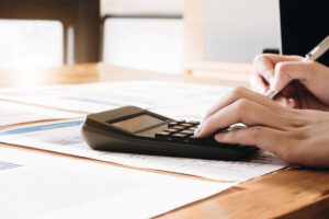 Close up of businesswoman or accountant hand holding pen working on calculator to calculate business data, accountancy document and laptop computer at office, business concept