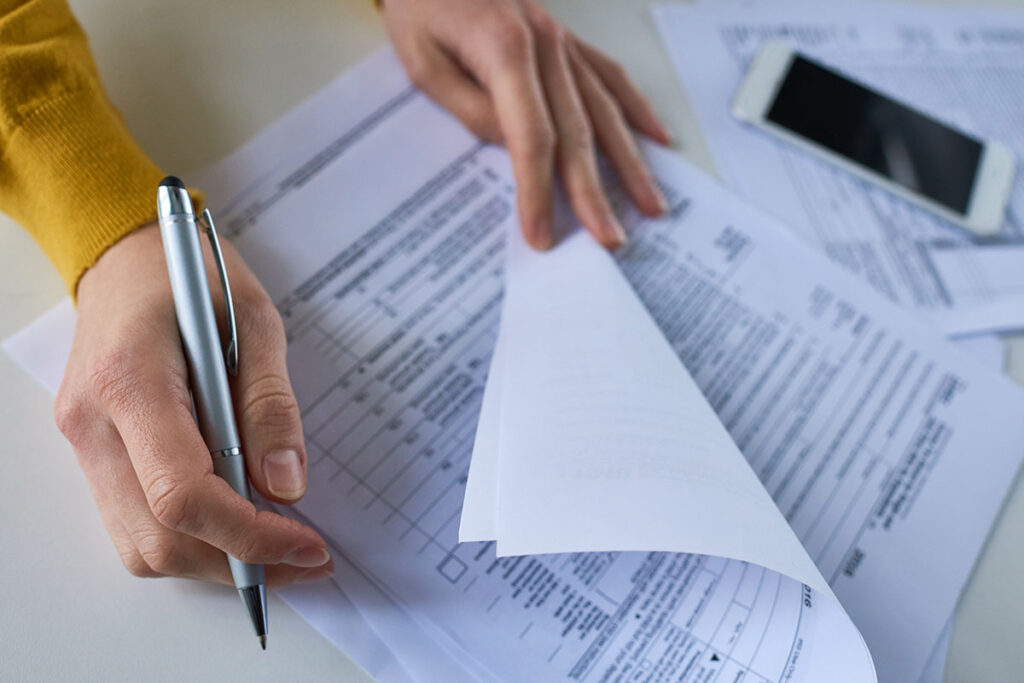 Close-up of unrecognizable woman attentively examining business documents and making correction at table