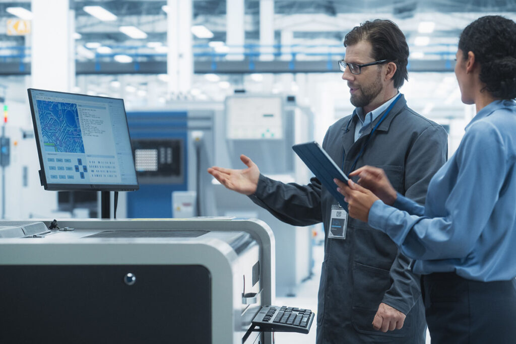 Caucasian Industrial Engineer And Hispanic Female Supervisor Using Tablet And Talking At Electronics Factory. Man Using Soldering Jet Printer, Explaining Process Behind Production Of New Microchips. - stock photo