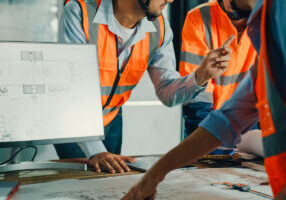 Closeup of team of industrial engineers meeting analyze machinery blueprints consult project on table in manufacturing factory