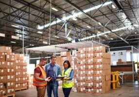 Shot of a group of coworkers talking together while standing in a large warehouse full of boxes