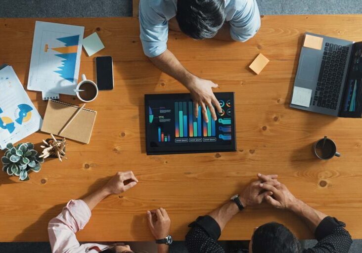 Top aerial view of business man present financial graph to group of smart investors. Professional male leader analyze graph and explain marketing idea by using tablet on meeting table.