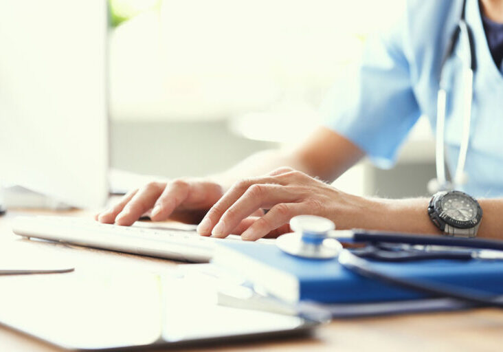 Medicine doctor's writing on keyboard in medical office close-up. Stethoscope, clipboard and notepad on foreground.